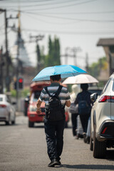 Fototapeta premium Man walking through city street holding umbrella, health safety and protection from heatstroke during heatwave, male hiding from sun under umbrella while passing by crossroad on hot summer day.