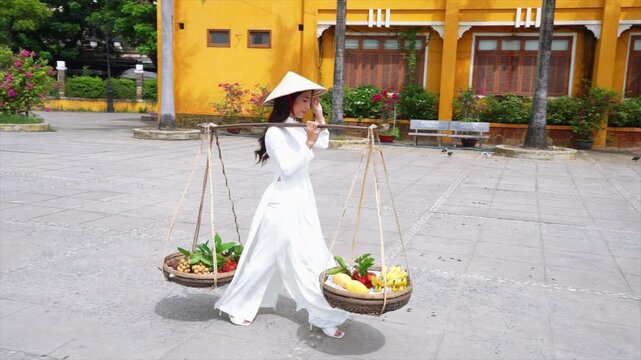 Vietnamese girl in an ao dai dress carries a fruit basket in Hoi an.