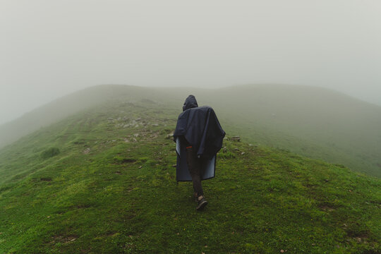 Hiker in a raincoat walking on a misty green mountain ridge in Ali Bedni Bugyal, Chamoli, Uttarakhand, India