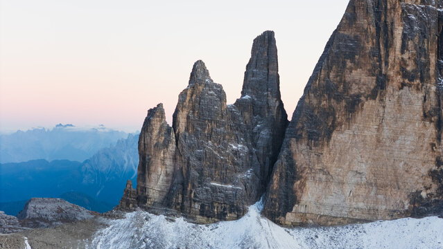 Aerial view of Tre Cime di Lavaredo peaks with snow-covered slopes and distant mountain ranges under a soft twilight sky Auronzo di Cadore, Veneto, Italy.