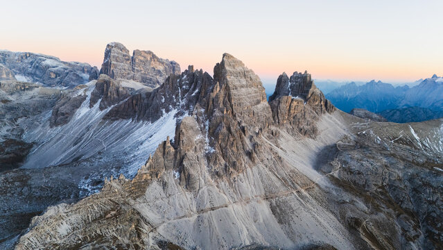 Aerial view of Tre Cime di Lavaredo with jagged peaks and snow-dusted rocky slopes under a soft dawn sky Auronzo di Cadore, Veneto, Italy.