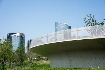 Obraz premium Modern concrete overpass in urban park with glass skyscrapers and blue sky