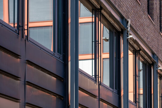 Warm glass reflection runs along a corporate building facade as urban architecture, windows, and abstract geometry catch evening light near brick walls