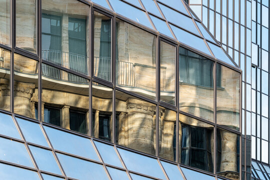 Historic reflection stretches through glass windows on a corporate building facade, where urban architecture meets abstract geometry and bright sky