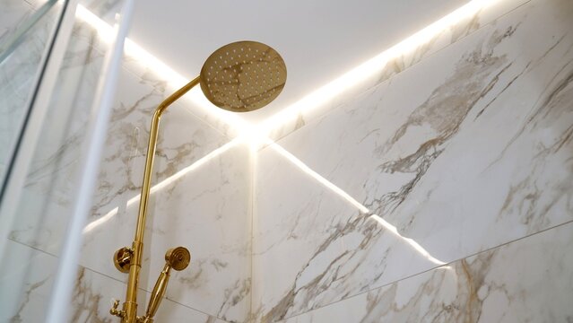 Modern gold shower head on white marble wall with glowing led strip lighting