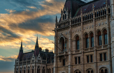 Obraz premium Majestic view of the Hungarian Parliament Building in Budapest at sunset with dramatic golden clouds over Gothic Revival architecture and historic stone facades