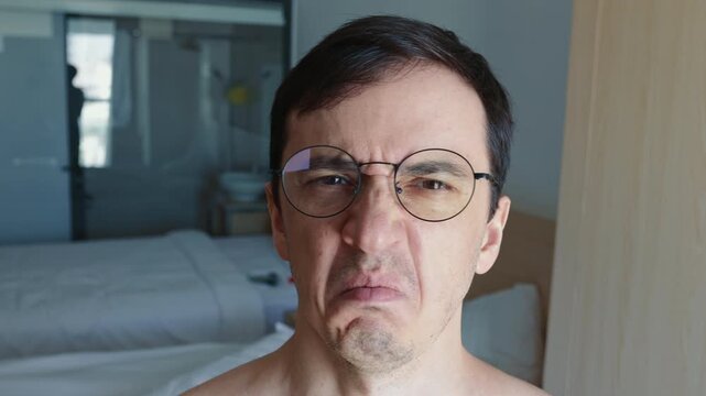 Mature man with glasses looking directly at the camera with a profound expression of disgust and aversion, wrinkling his nose and frowning in a strong display of negative emotion
