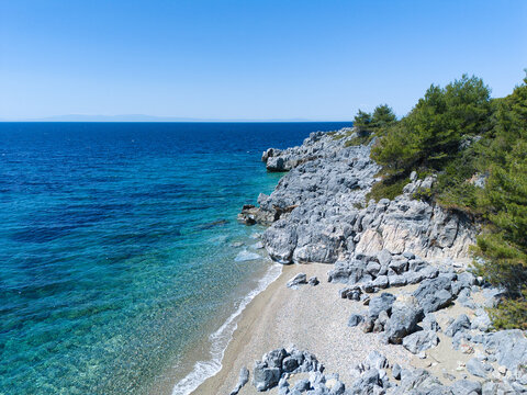 Aerial view of a secluded pebble beach and rugged rocky cliffs meeting the turquoise Aegean Sea under a clear blue sky Pallini, Greece.