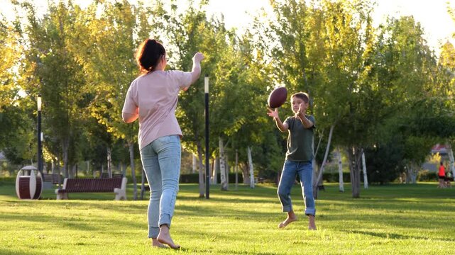 Mother and son playing casual ball game in park at sunset, running and passing ball in golden light. Concept of playful training, child development and active lifestyle, energetic outdoor sports