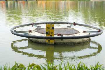 Obraz premium A yellow water level gauge installed on a concrete drainage structure in a pond. Concept of water management, flood monitoring, and irrigation infrastructure.
