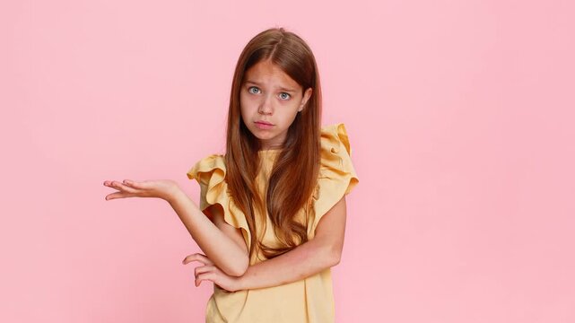 Young child girl raises eyebrows in confusion, showing hand gesture meaning what, why, expressing surprise and curiosity. School kid isolated on pink background with emotional and playful reaction.