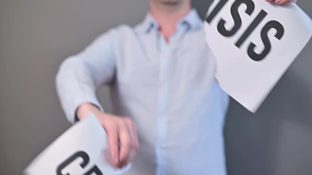 A person is shown in a series of actions involving paper signs with the word Crisis. The individual tears and presents parts of the signs, conveying a message about urgency and concern