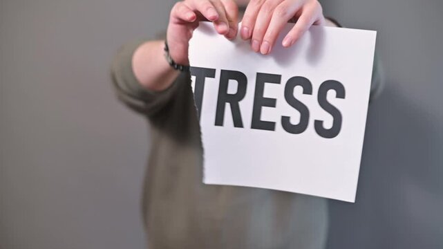 A man is seen holding a sign with the word stress clearly visible and then proceeds to tear it in half. This action symbolizes the concept of releasing and managing stress in daily life situations