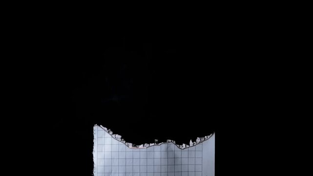 Smoke rises slowly from the charred and smoldering edge of squared graph paper against a completely dark black background. Concept of destroyed evidence, lost memories, or abandoned ideas.