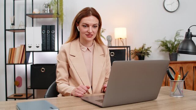 Middle-aged businesswoman at home office on laptop joins video lecture in earphones nods answers chat explains points. Freelancer girl at table runs interview in video chat thanks audience posts notes