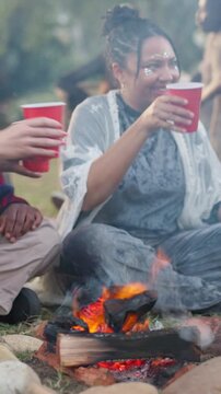 Festival, friends and woman with toast by bonfire, weekend celebration and bonding at social event. Cheers, reunion and happy people with alcohol drinks for summer break, outdoor or gathering for fun