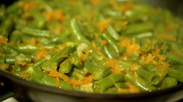 Fresh green beans and grated carrots simmer with steam rising in a hot frying pan. Concept of healthy eating, vegetarian cooking, homemade diet, and nutritious meal prep.