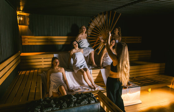 Female sauna master performing an aufguss ritual with a fan for a diverse group of women during a girls getaway