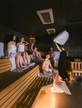 Male sauna master waving a towel during an aufguss ritual for a group of young people in a large dry sauna