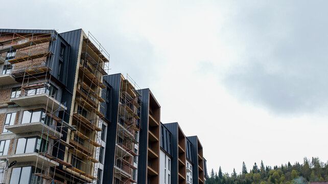 Modern apartment building under construction with scaffolding and forest backdrop