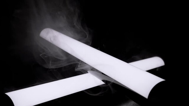 White smoke drifts smoothly over two crossed cylinders isolated against a pure black background. Concept of abstract mystery, atmospheric mood, and modern minimalist design.