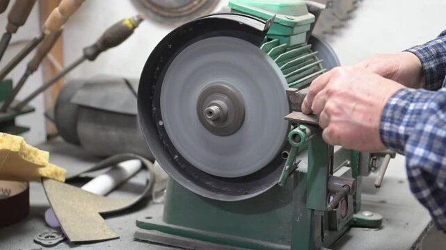 A desktop metal sharpening and grinding machine is in operation. Working hands sharpen a metal part on a desktop electric grinding machine