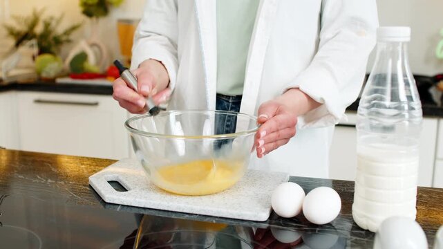 Unrecognizable woman whisking eggs in bowl for omelet breakfast in home kitchen for healthy diet. Unrecognizable girl cooking indoors feeling happy choosing simple nutrition lifestyle for weight loss.
