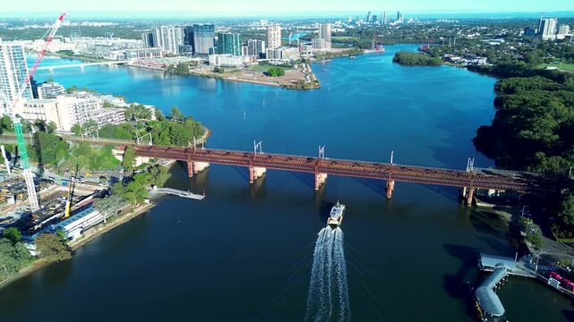 Drone aerial landscape of passenger ferry cruising underneath Parramatta River railway bridge surrounded by urban waterfront buildings in Rhodes Sydney city NSW Australia transportation infrastructure