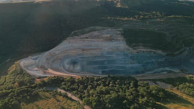 Expansive limestone and cement mining quarry carved into the hillside Distrito Federal, Brazil surrounded by green vegetation and native forest borders, drobe orbit establishing shot