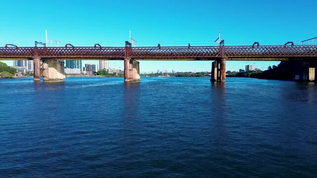 Drone aerial landscape of Parramatta River railway train-line bridge near the waterfront boardwalk reserve in Meadowbank with urban buildings in the background of Sydney NSW Australia infrastructure