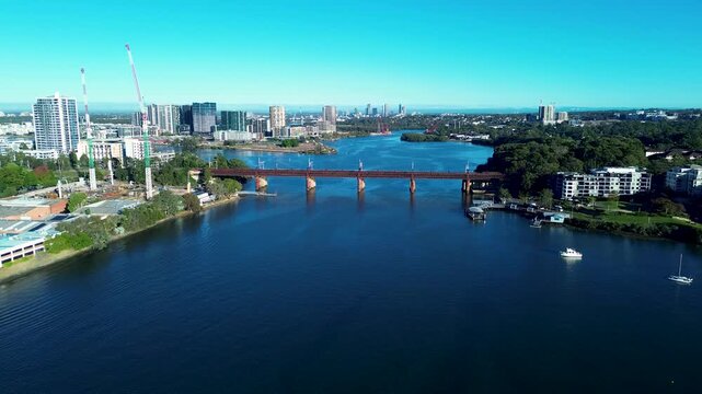 Drone aerial landscape of Parramatta River railway bridge surrounded by urban buildings and construction cranes along the waterfront pier reserve near Meadowbank Sydney city Australia infrastructure
