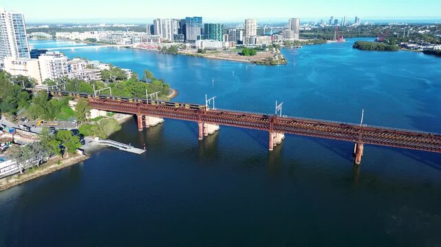 Drone aerial landscape of commuter train passing along the Parramatta River railway bridge tracks into the suburb of Rhodes surrounded by urban buildings near Meadowbank Sydney city Australia travel