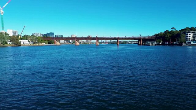 Drone aerial landscape of water surface with Parramatta River railway train bridge surrounded by urban waterfront buildings along the reserve in Meadowbank Sydney city Australia tourism and marine
