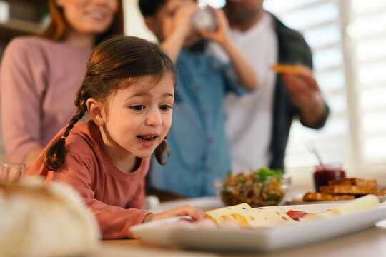 Curious little girl reaching for food during family breakfast