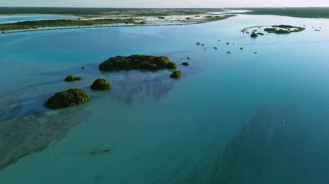 Aerial drone shot orbiting right and descending over ancient stromatolites and Isla de los Pajaros with sailboats in Bacalar Lagoon at golden hour sunset Mexico.