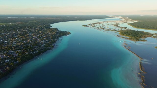 Aerial drone panoramic shot of the town of Bacalar Lagoon and green mangroves showing abstract turquoise patterns during sunset Mexico.