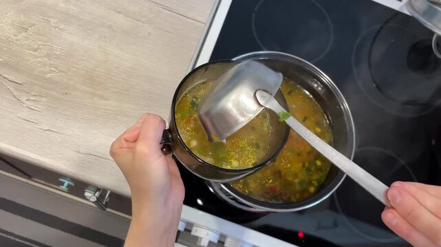 Soup serving scene, Steaming vegetable broth placed into bowl, Family enjoying warm vegetable soup in cozy kitchen, Closeup of ladle pouring colorful vegetable soup into bowl for family dinner