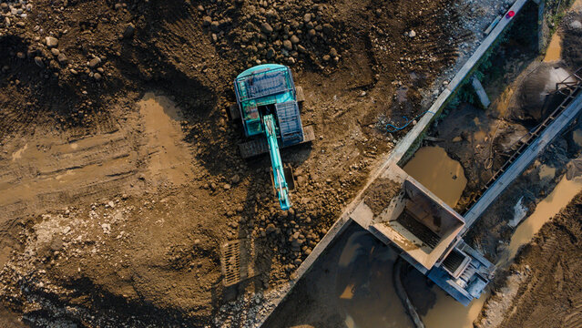 Excavator in Mining Quarry and Rock Crusher Facility on Sunny Day, Industrial mining site captured from above, featuring heavy machinery, material processing operations, rugged excavation terrain