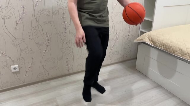 Indoor basketball juggling. Individual performing balance and coordination drills with basketball indoors. Solo athlete practicing ball handling and balancing exercises in cozy indoor environment