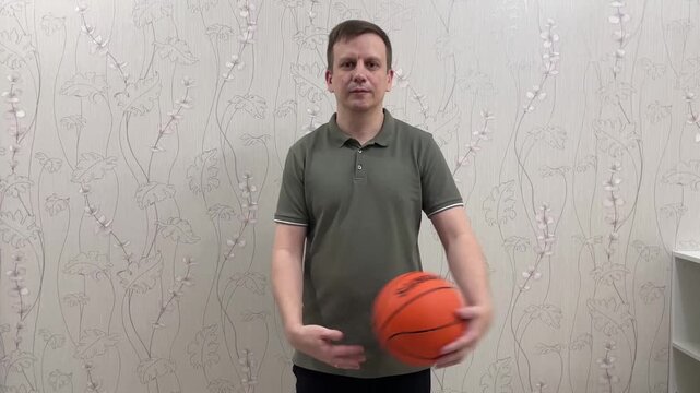 Man holding basketball at side in front of patterned wall, demonstrating stance and hand placement, approachable expression, midshot with simple indoor setting, practice sequence and coaching tone