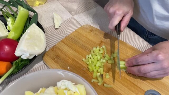 Chopped celery added, Finely diced celery incorporated into potato salad mixture, Celery has been meticulously chopped and blended into potato salad mixture for flavor and texture enhancement