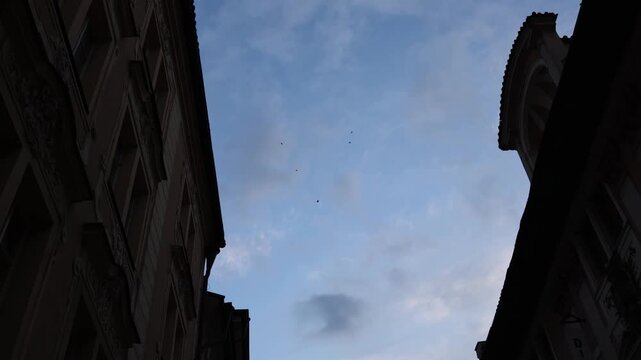 Paratroopers flying above narrow historic street between old European buildings during evening airborne demonstration and tactical aerial event