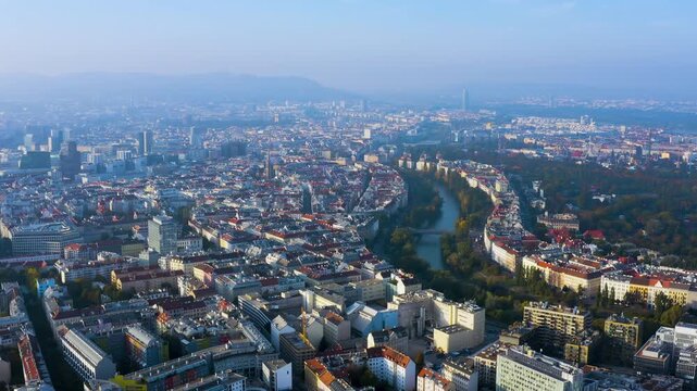4K aerial wide view of Vienna's dense Habsburg cityscape with the Donaukanal curving toward the Prater and Wienerwald hills shrouded in hazy autumn morning light.