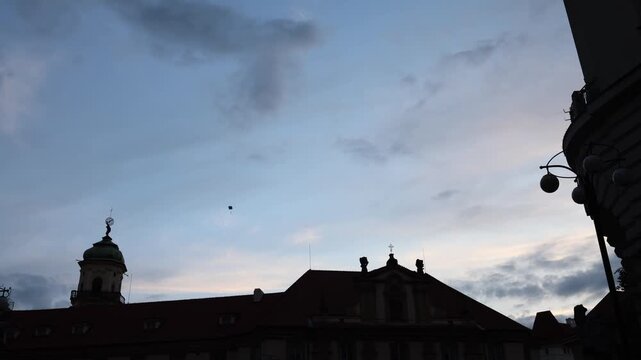 Stormy evening sky above historic European rooftops while parachutist slowly descends over old city center during public aerial performance event