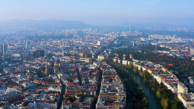 4K aerial view across Vienna's Leopoldstadt district with the Donaukanal, Prater Giant Ferris Wheel, DC Tower and Vienna Woods on the hazy autumn morning horizon.