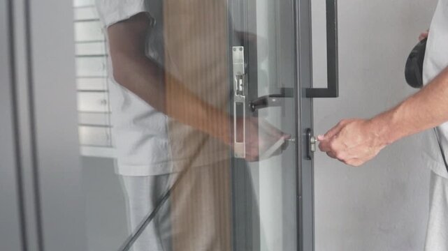 Close-up of a man opening an apartment building entrance door with keys. Cropped lifestyle scene showing a male hand unlocking a modern glass door in a residential building