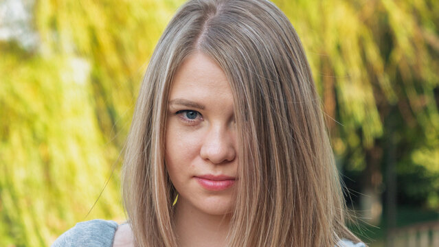 Headshot of a young woman with straight light blonde hair and blue eyes outdoors in natural light