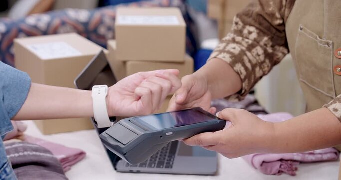 Senior asian woman entrepreneur holds POS terminal as customer uses smartwatch payment, artisan online seller handles order paperwork on laptop, supports business logistics, parcel shipping delivery.