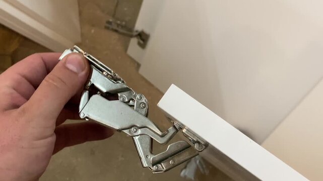 Modern concealed metal hinge installed on a white furniture cabinet door. Close-up view.
