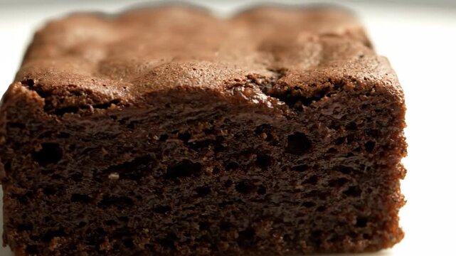 Decadent Chocolate Brownie Macro Shot. Extreme Close-up of Rich, Fudgy Dessert Square Showing Moist Texture and Cracked, Dark Brown Crust on a White Background.